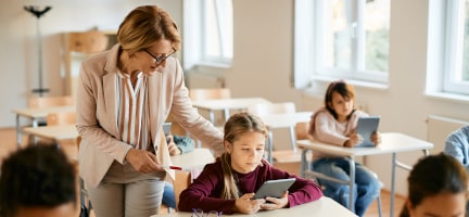 Docente apoyando a una alumna durante una actividad con tablet en el aula, representando la formación digital y el aprendizaje con nuevas tecnologías en entornos educativos.