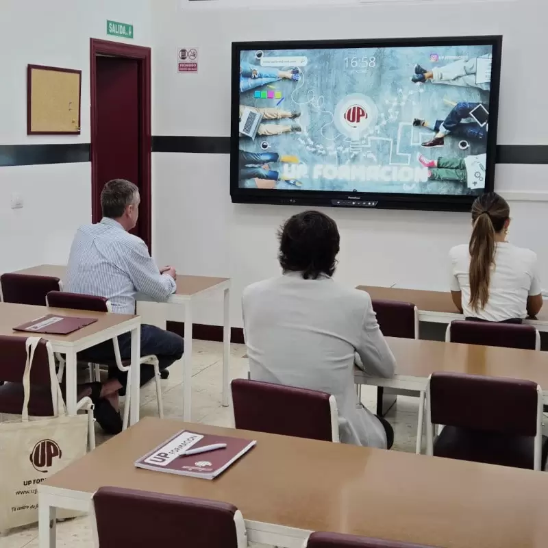 Alumnos asistiendo a una clase presencial en un aula de UP Formación, siguiendo la sesión en una pantalla interactiva dentro de un entorno de formación profesional en Bilbao.